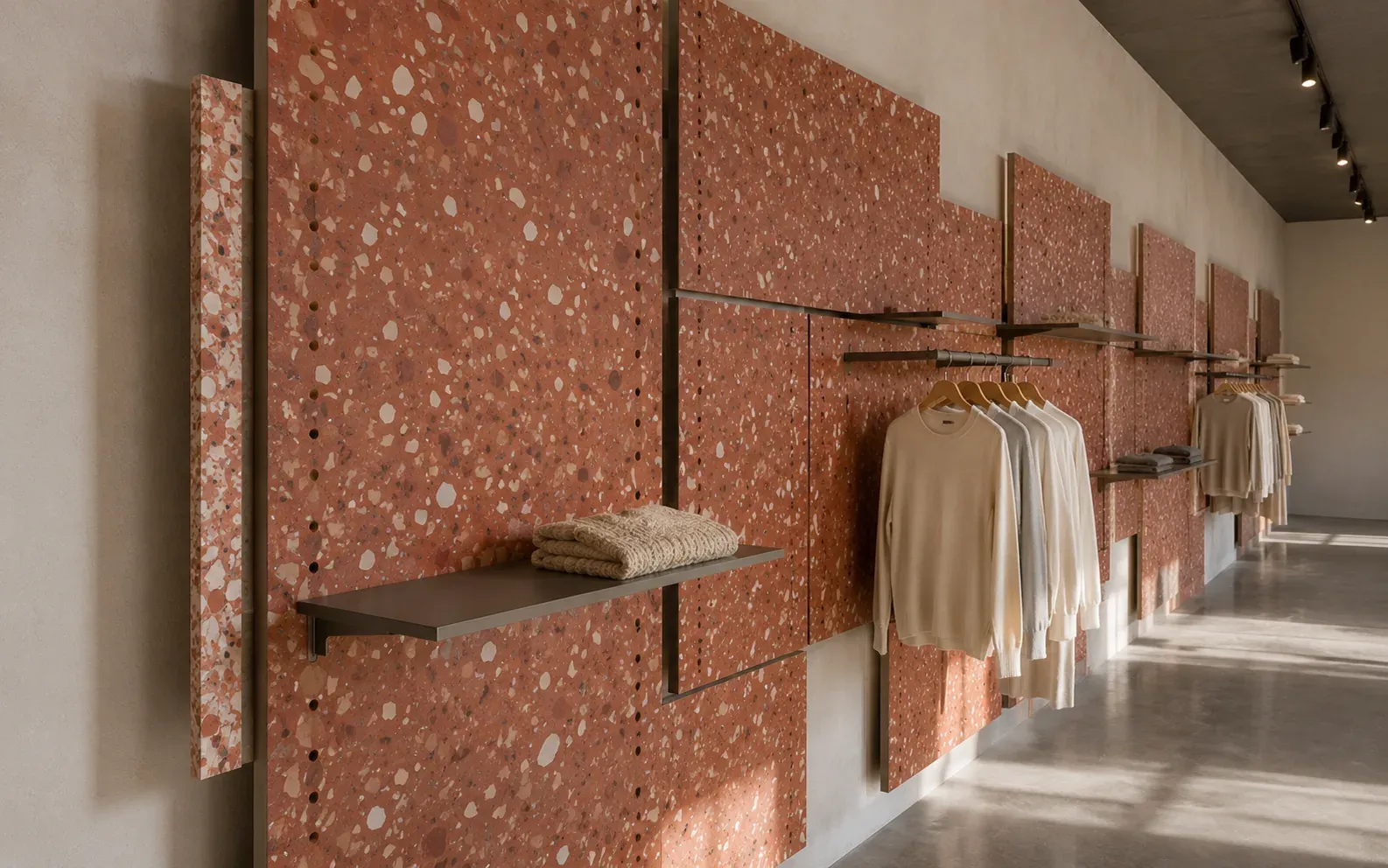 Parete espositiva del flagship Corda a Verona: pannelli Sedimento nella finitura Ossido, rosso con scaglie chiare in vista, forati su passo 32 mm e staccati dal muro, con mensole e un'asta appendiabiti agganciate ai fori; in primo piano un pannello di taglio mostra le scaglie nello spessore